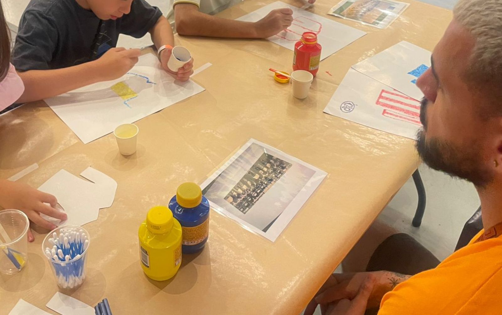 imagem - foto da tividad Oficina de Pontilhismo. N amesa o educador ensina crianças a atividade