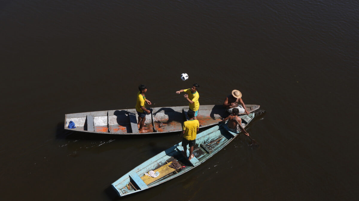 Ribeirinhos com a bola oficial Telstar da Copa da Rússia de 2018 no Igarapé Açu em Manacapuru Municipio do Amazonas. Eles estão em canoas e são fotografados de cima. Três deles jogam bola com a camisa do Brasil. Outros dois esteão sentados e parecem conversar à frente dos barcos.