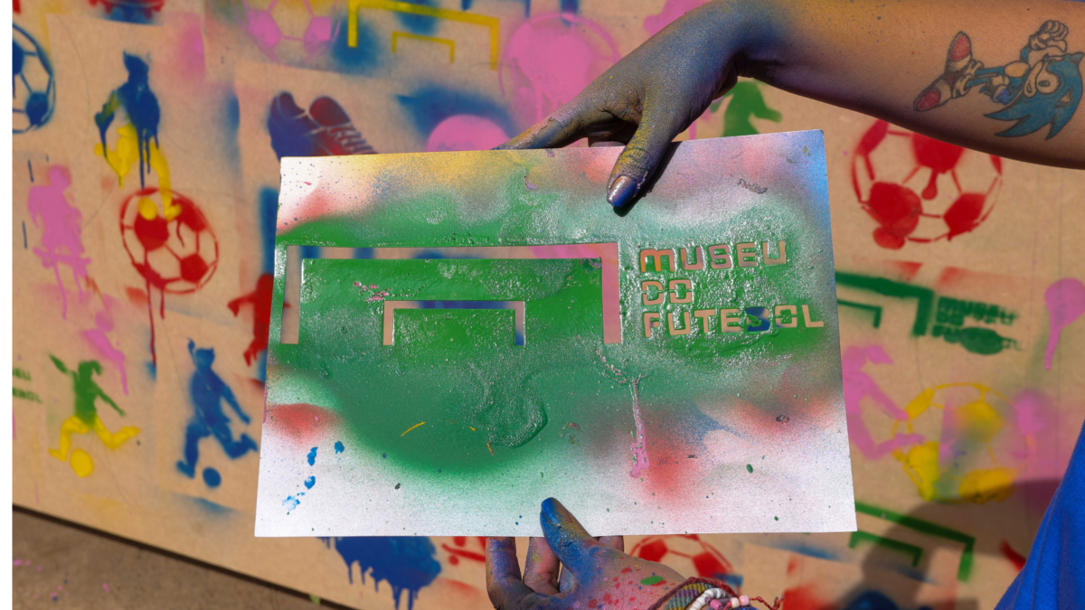 imagem de um muro pintado em grafite. uma mão segura um desenho em grafite e nele está escrito: Museu do Futebol.