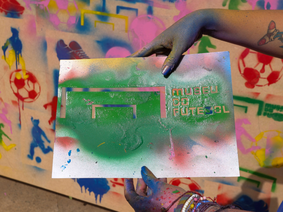 imagem de um muro pintado em grafite. uma mão segura um desenho em grafite e nele está escrito: Museu do Futebol.